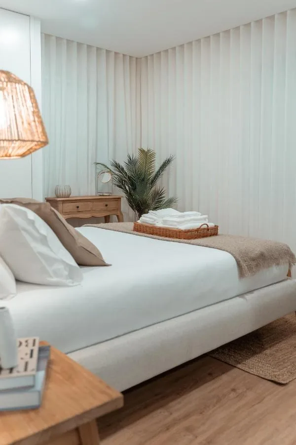 Quarto principal do Apartamento T2 — cama em linho branco, cortinados em linho, candeeiro em rattan